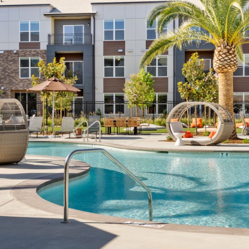 Refreshing moments await in your community pool Elegant apartment complex in Sacramento with resort-style pool, modern loungers, and lush palm trees, perfect for luxury living.