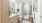 Elegant bathroom with modern wooden cabinetry, dual sinks, and a cozy bathtub with beige curtains. Features decorative artwork on the wall and lush greenery accents at Ona Natomas