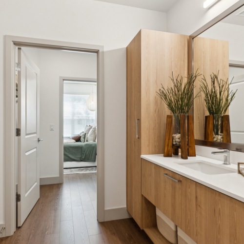 Spa-inspired bathrooms with modern finishes Modern apartment bathroom at Ona Natomas with sleek wooden cabinetry in the bathroom, leading to a cozy, sunlit bedroom in the background.