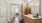 Modern apartment bathroom at Ona Natomas with sleek wooden cabinetry in the bathroom, leading to a cozy, sunlit bedroom in the background.