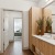 Modern apartment bathroom at Ona Natomas with sleek wooden cabinetry in the bathroom, leading to a cozy, sunlit bedroom in the background.