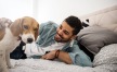 man smiles and pets his dog on a bed